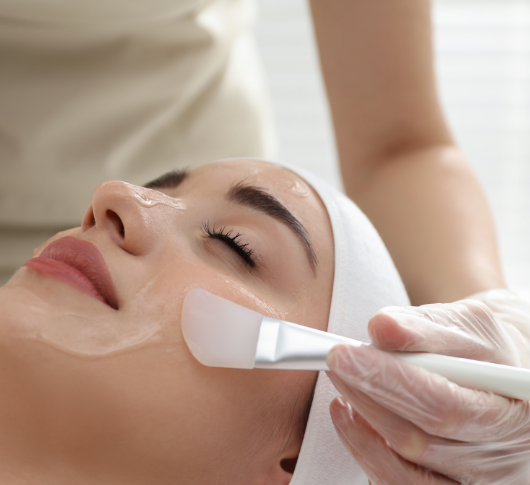 Gloved hands spread chemical peel on cheek