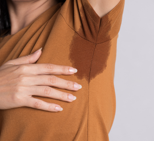 Brown sweat stain visible on orange top under woman’s armpit