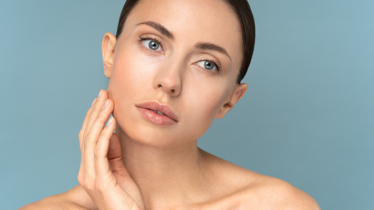 Woman with clear skin touching her face on blue background